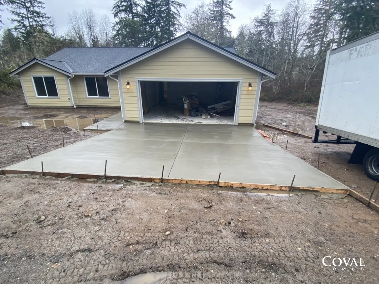 Single-story yellow house with open garage and new concrete driveway in a wooded yard