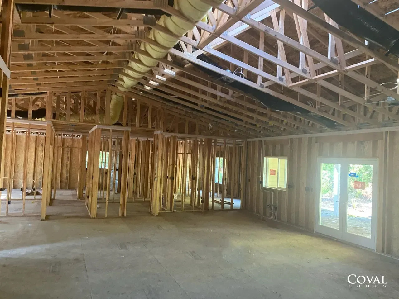 Unfinished house interior with exposed wooden framing, trusses, and bright windows.