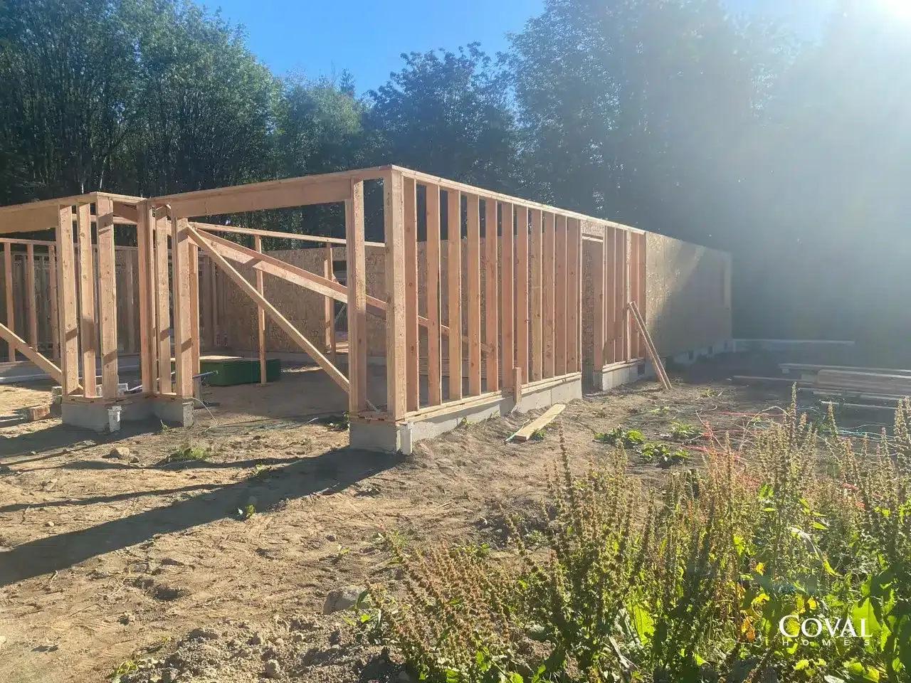 Partially framed wooden house foundation on a dirt lot under clear blue sky