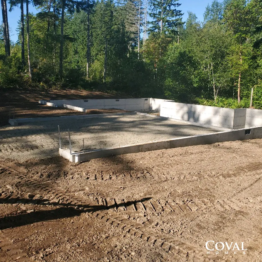 Concrete foundation under construction in a wooded area with dirt foreground and bright sunlight