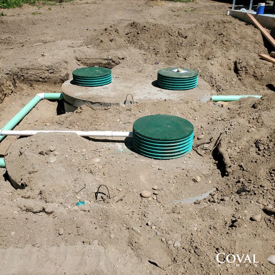 Three green septic tank risers and white pipes installed in a dirt excavation site.