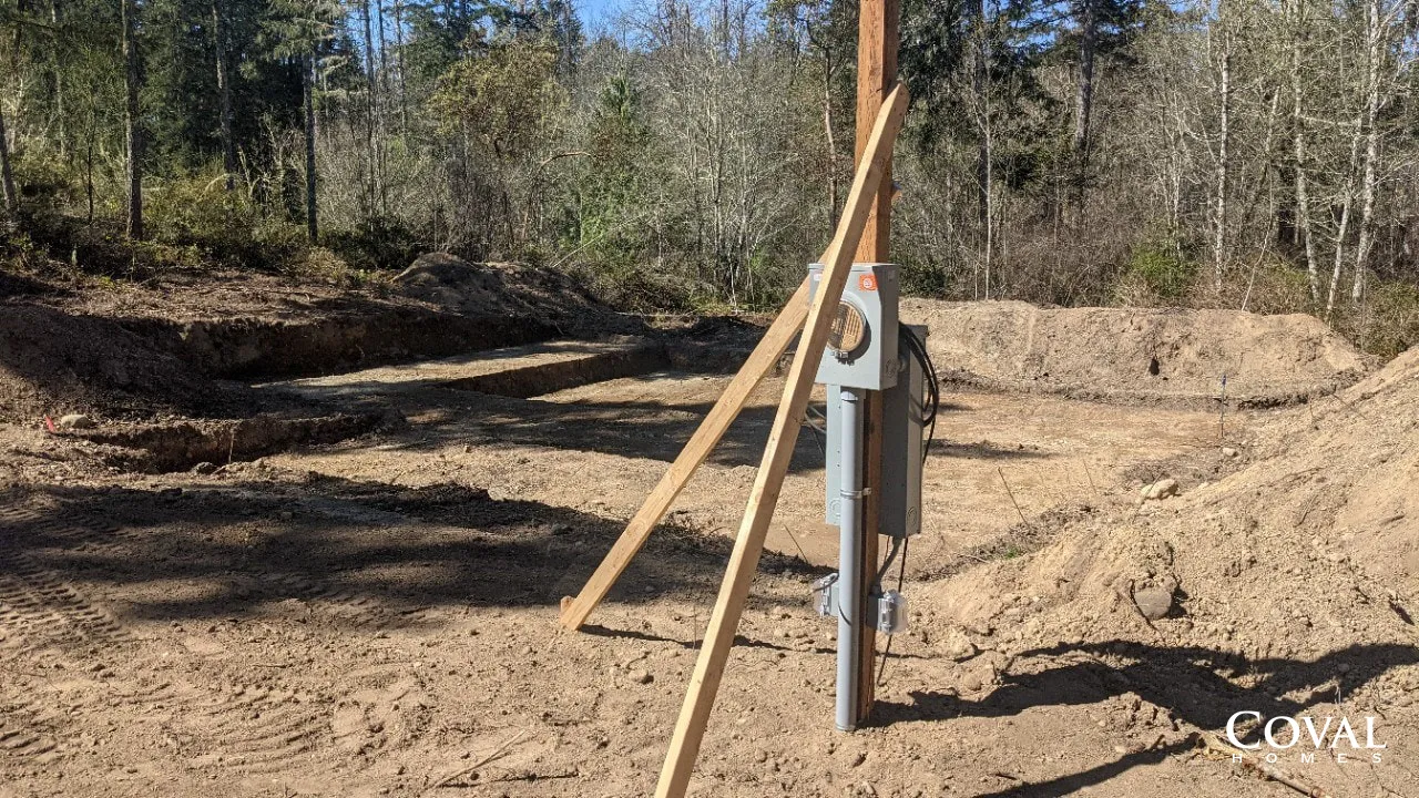 Surveying equipment on a dirt construction site with wooden stakes and a wooded background