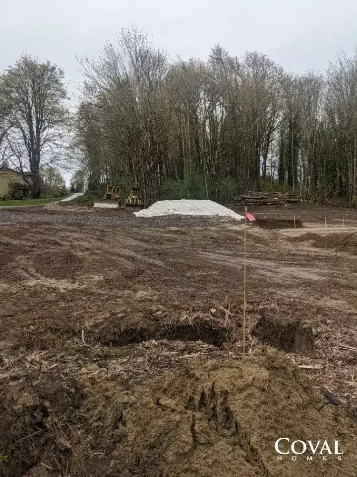 Muddy construction site with a white gravel pile and trees in the background