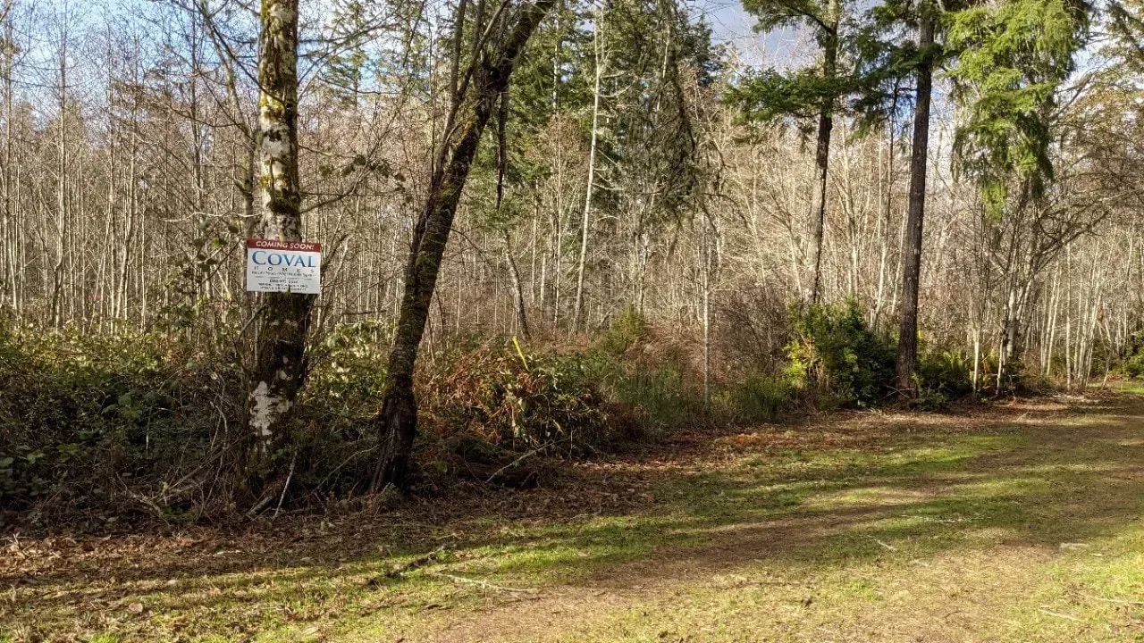 Wooded trail with a posted sign on a tree and a grassy clearing in the foreground