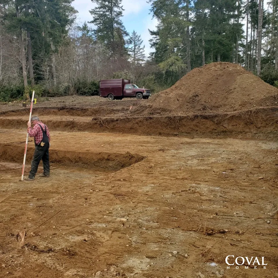 Person with a survey pole in a dirt clearing near a red truck and large soil mound in a wooded area