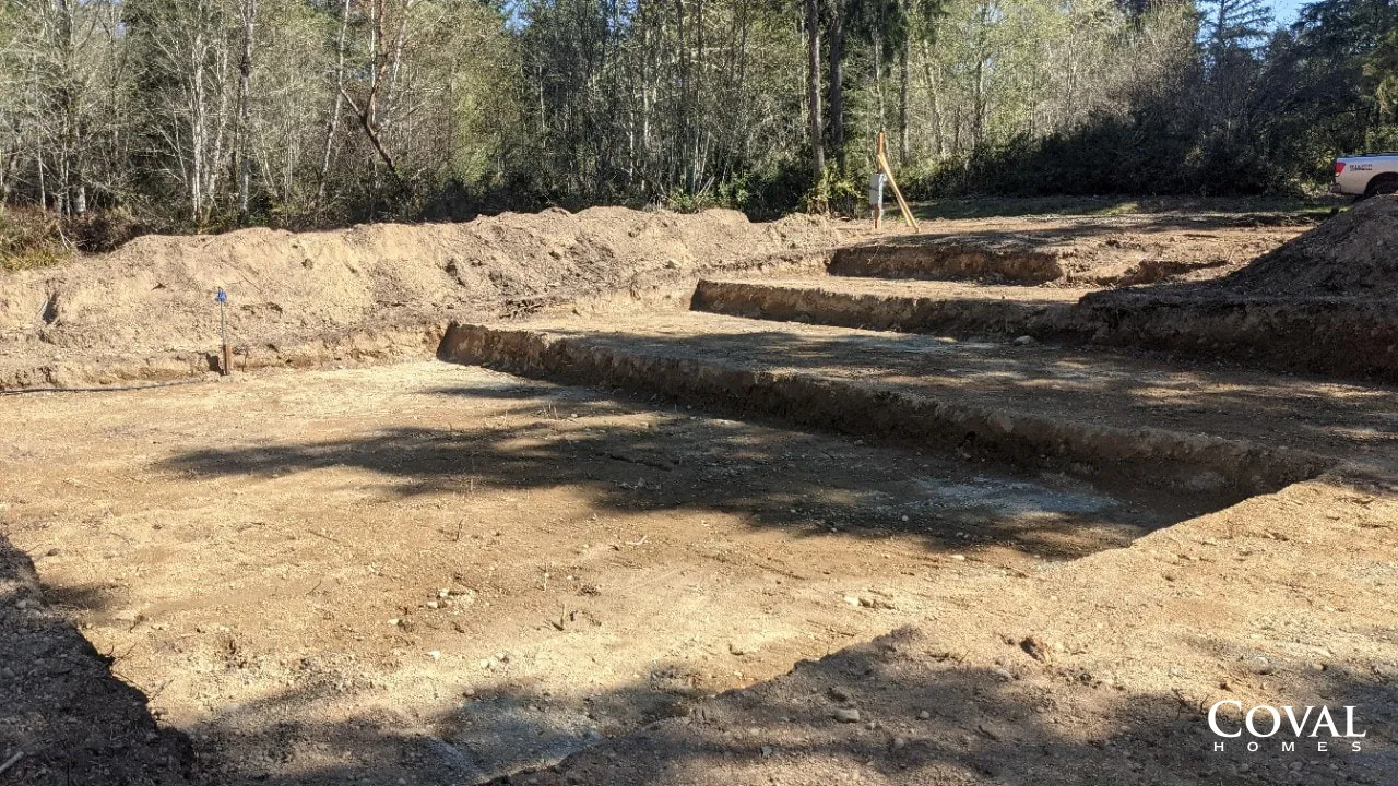 Excavated dirt lot with leveled soil and piles of earth beside a wooded area