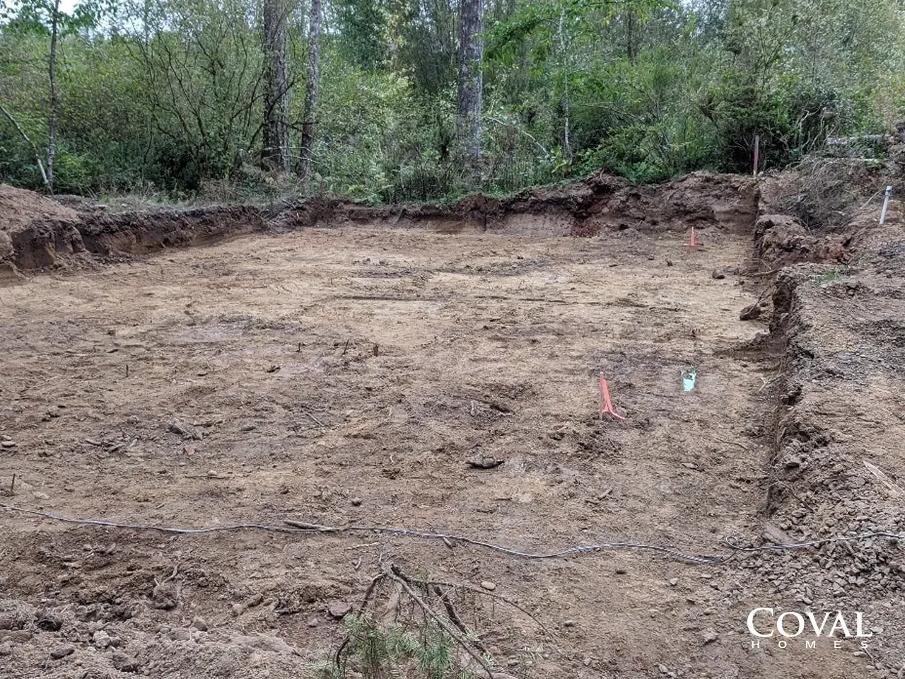 Cleared dirt lot in a wooded area, with stakes marking the ground and a COVAL watermark.
