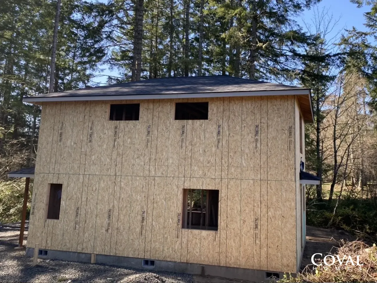Two-story house with light siding and small windows in a wooded area