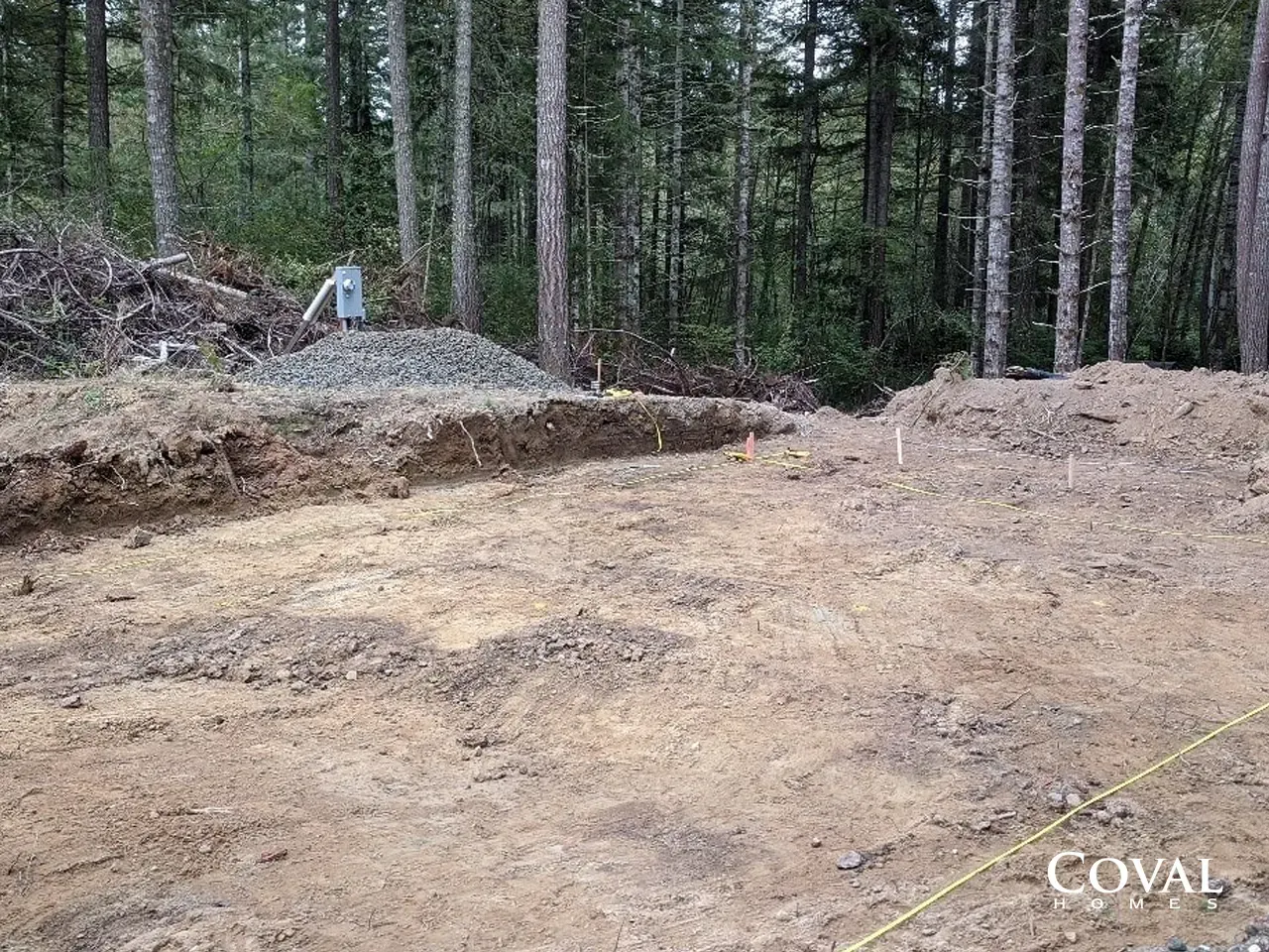 Cleared dirt lot in a wooded area, with piles of soil and gravel near tall pine trees