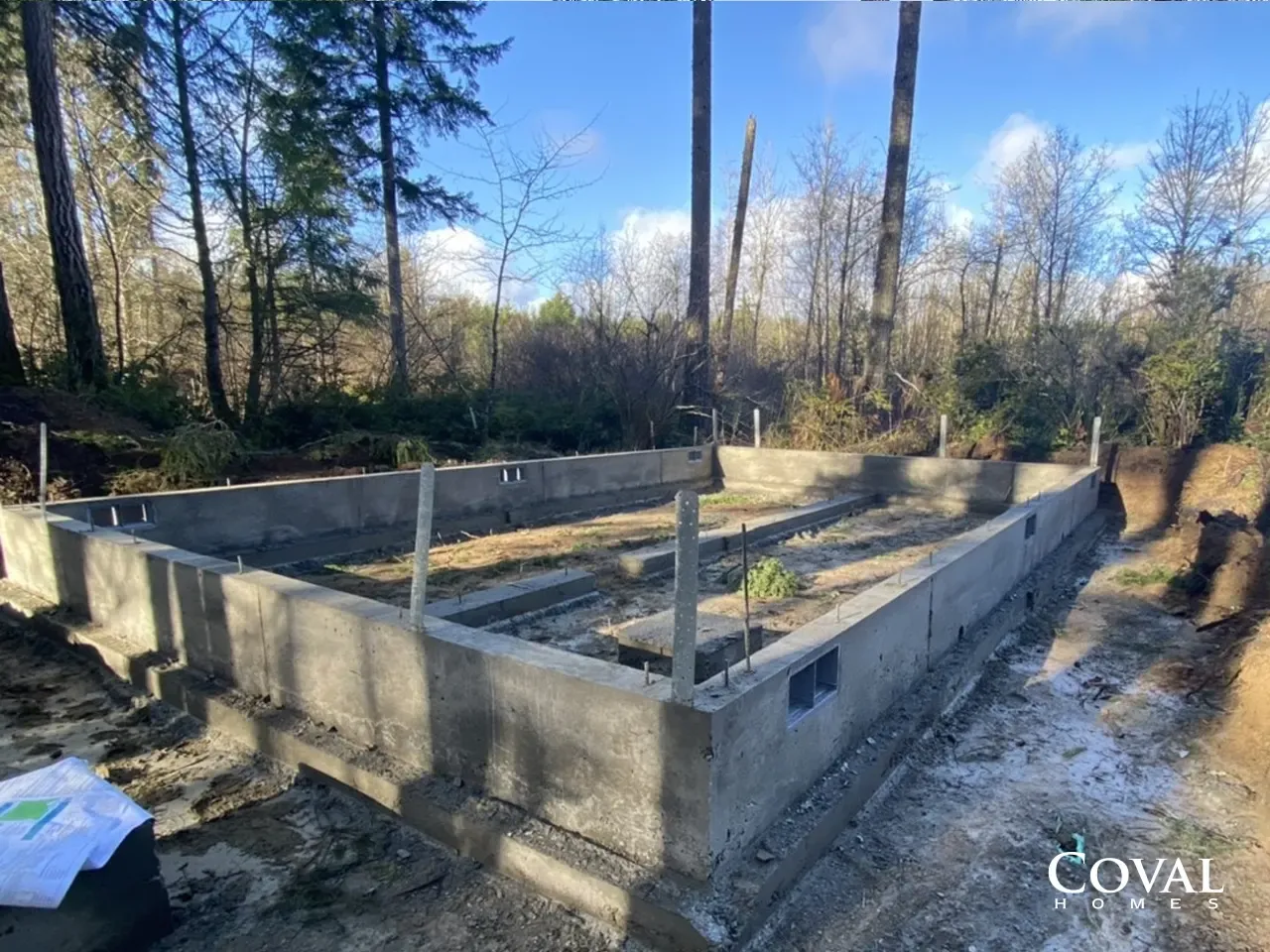 Concrete foundation in a wooded area with rebar posts under a blue sky.