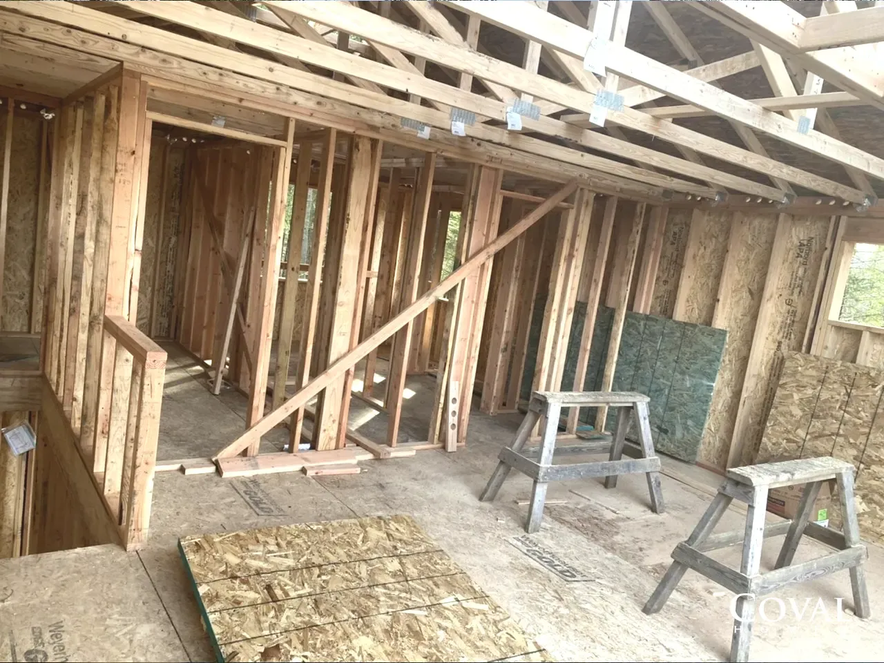 Interior of a room under construction with exposed wood framing, sawhorses, and a ladder