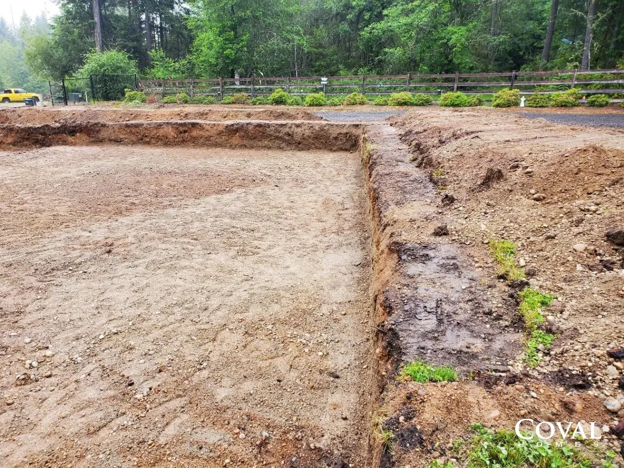 Cleared dirt lot with a narrow trench and green trees in the background