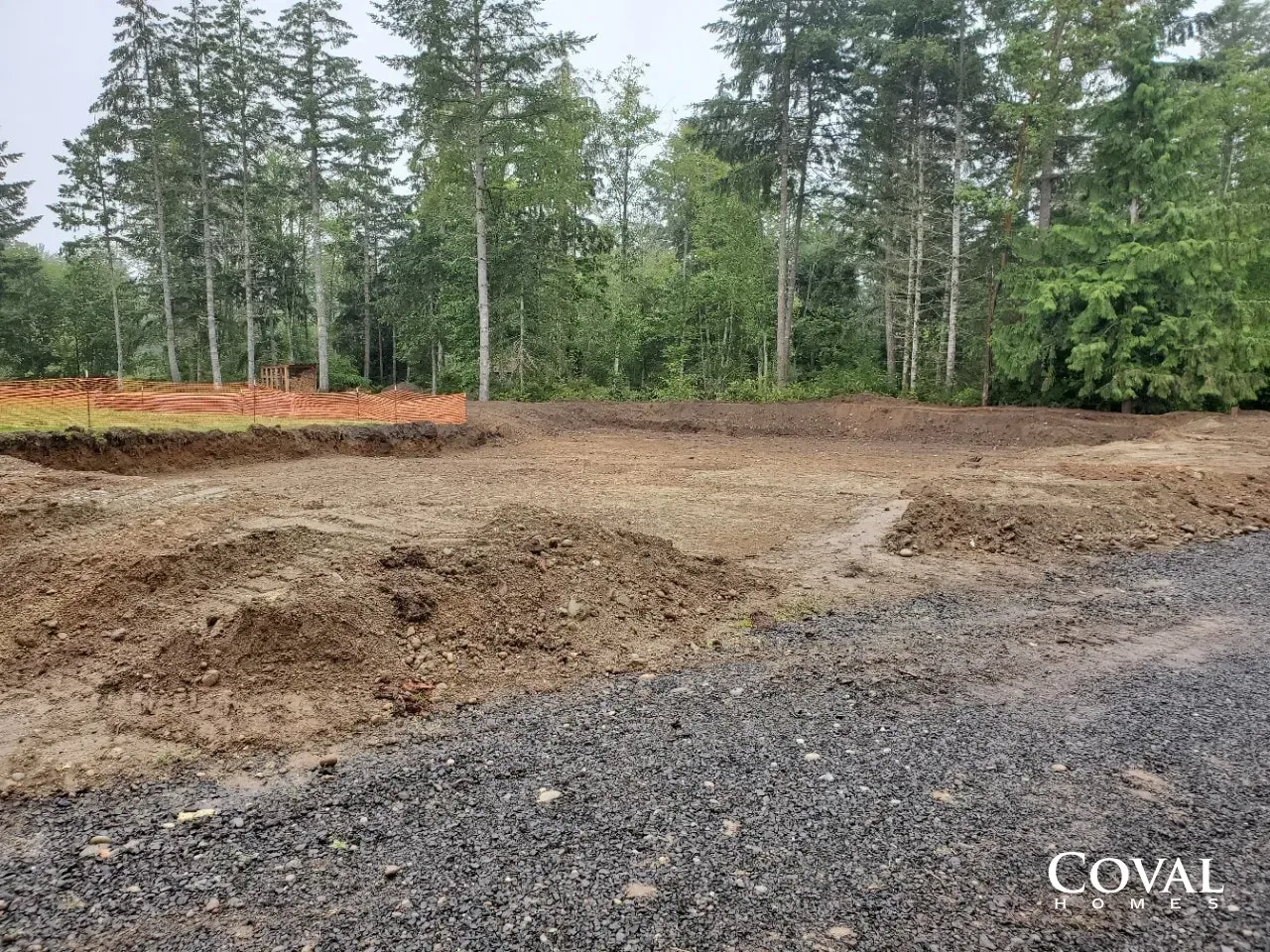 Cleared dirt lot with gravel foreground and trees in the background under overcast sky
