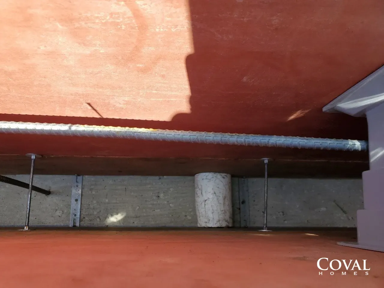 Close-up of a metal rail with two bolts on a red surface and concrete blocks below