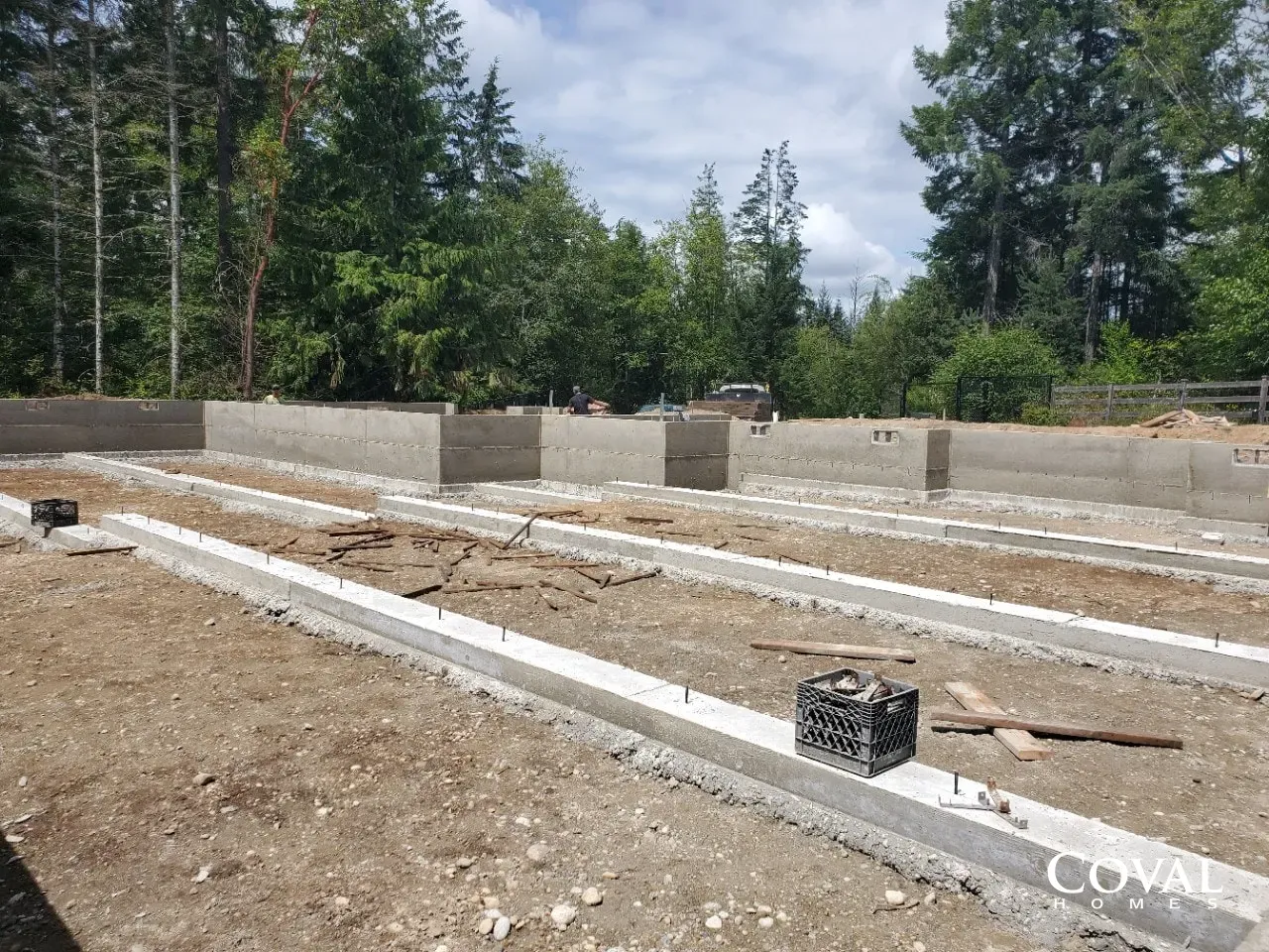 Foundation footings and concrete block walls at a wooded construction site under cloudy skies