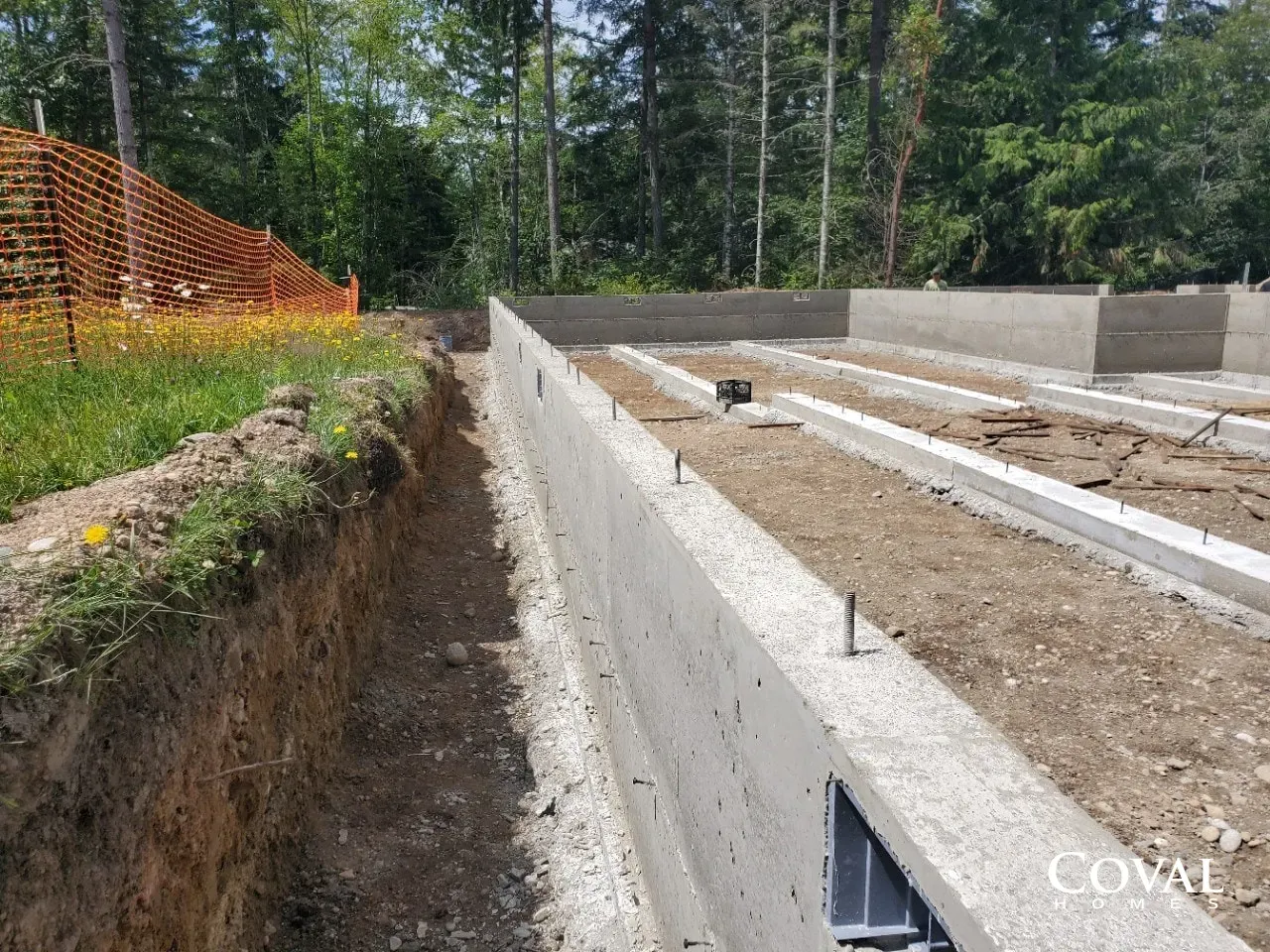Concrete foundation trenches and retaining walls at a construction site near a wooded area