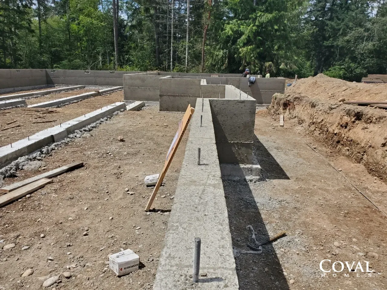 Concrete foundation walls under construction on a dirt lot with lumber and rebar