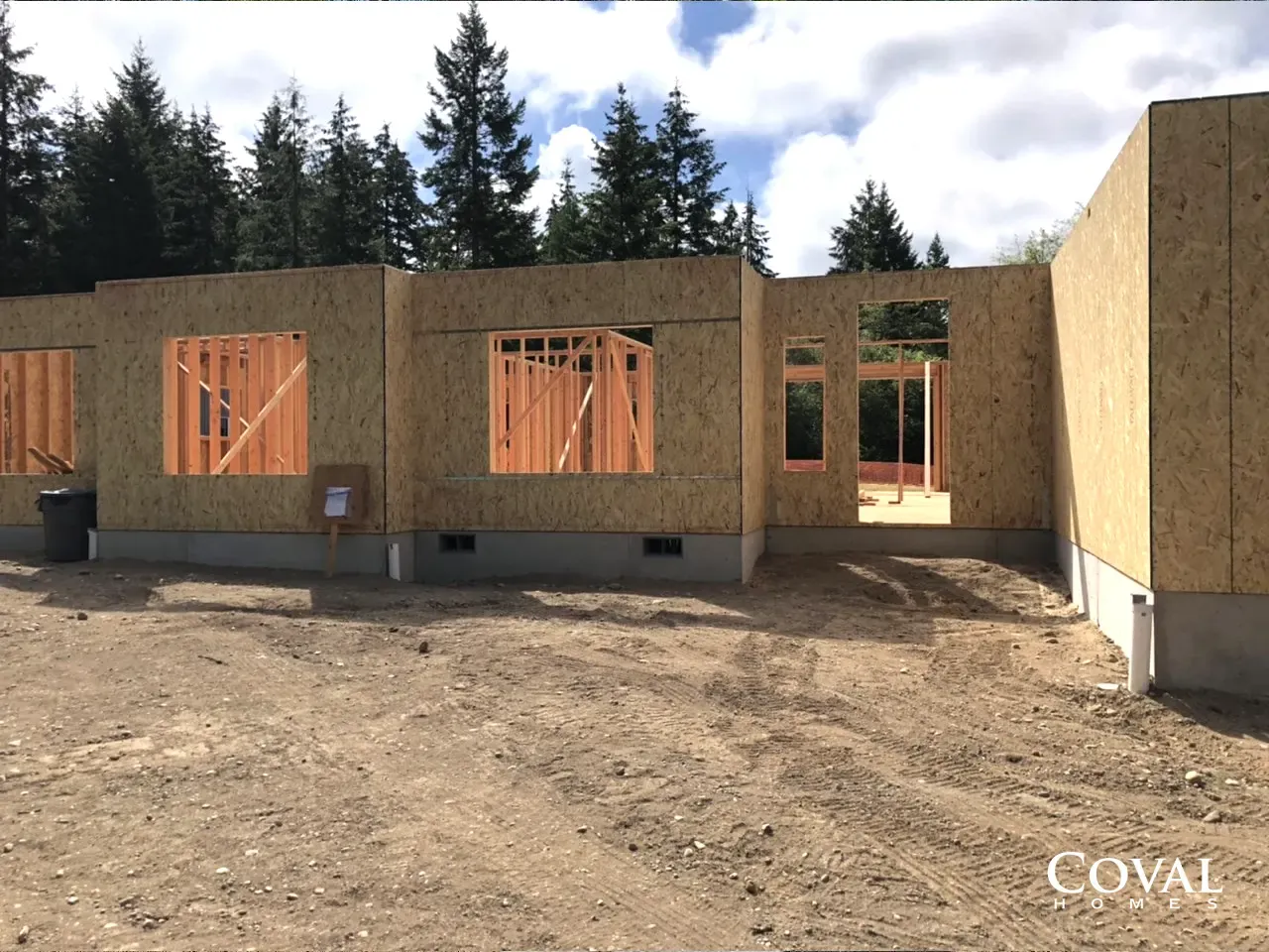 Partially built wooden house framing on a dirt lot under a cloudy sky
