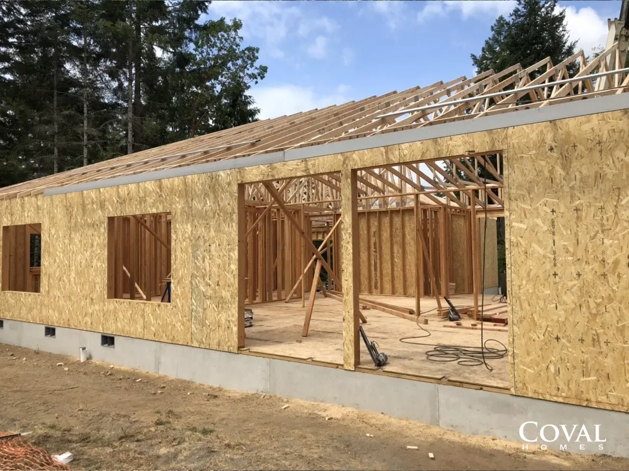 Partially built house with plywood sheathing and exposed roof framing on a concrete foundation