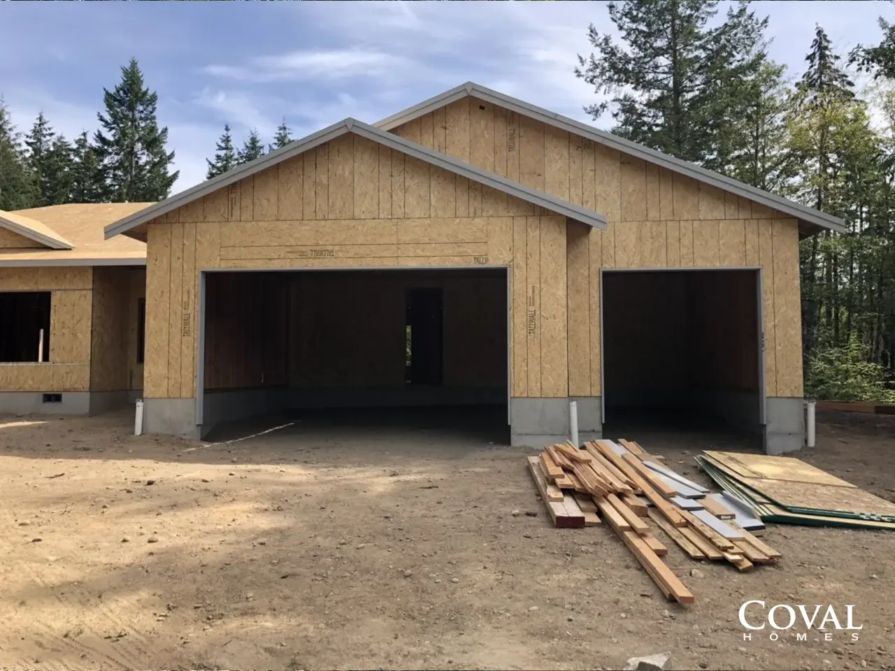 Unfinished wood-framed garage under construction with two open bays and lumber stacked in front