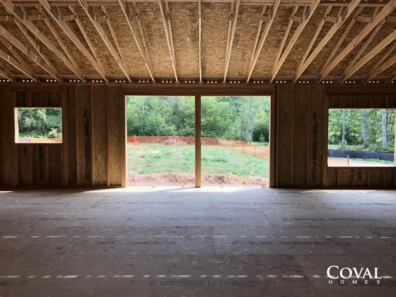 Empty wooden room under construction with open window and door openings overlooking green trees