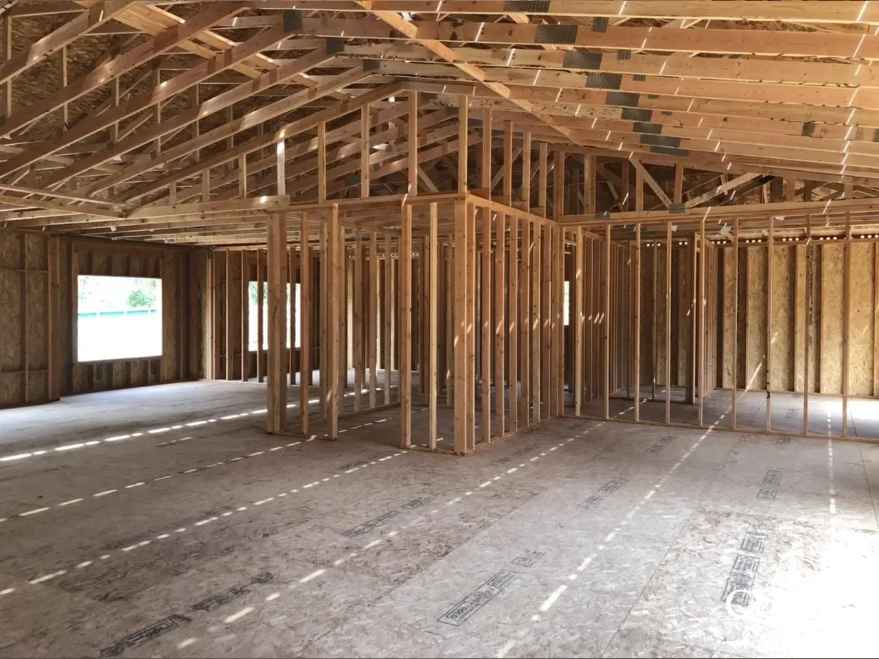 Unfinished wooden house interior with exposed framing, roof trusses, and subflooring