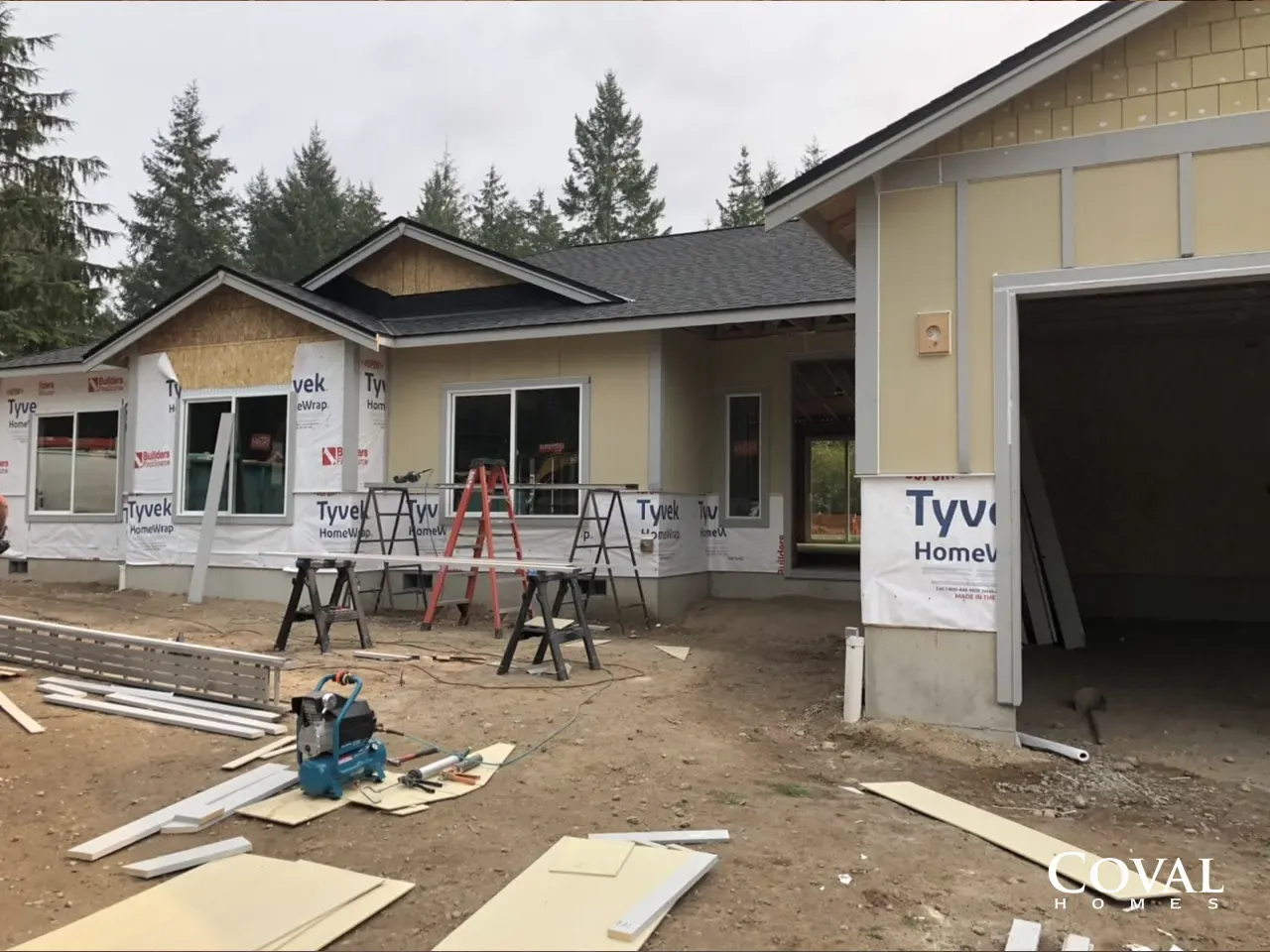 New home under construction with workers, ladders, building materials, and open garage