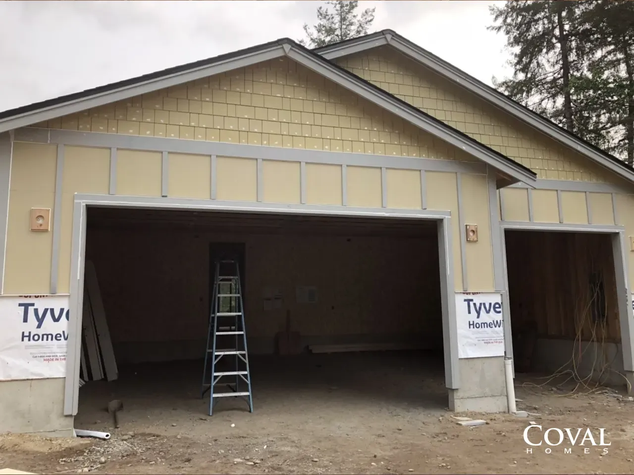 House under construction with open garage, ladder inside, and Tyvek wrap on the sides.