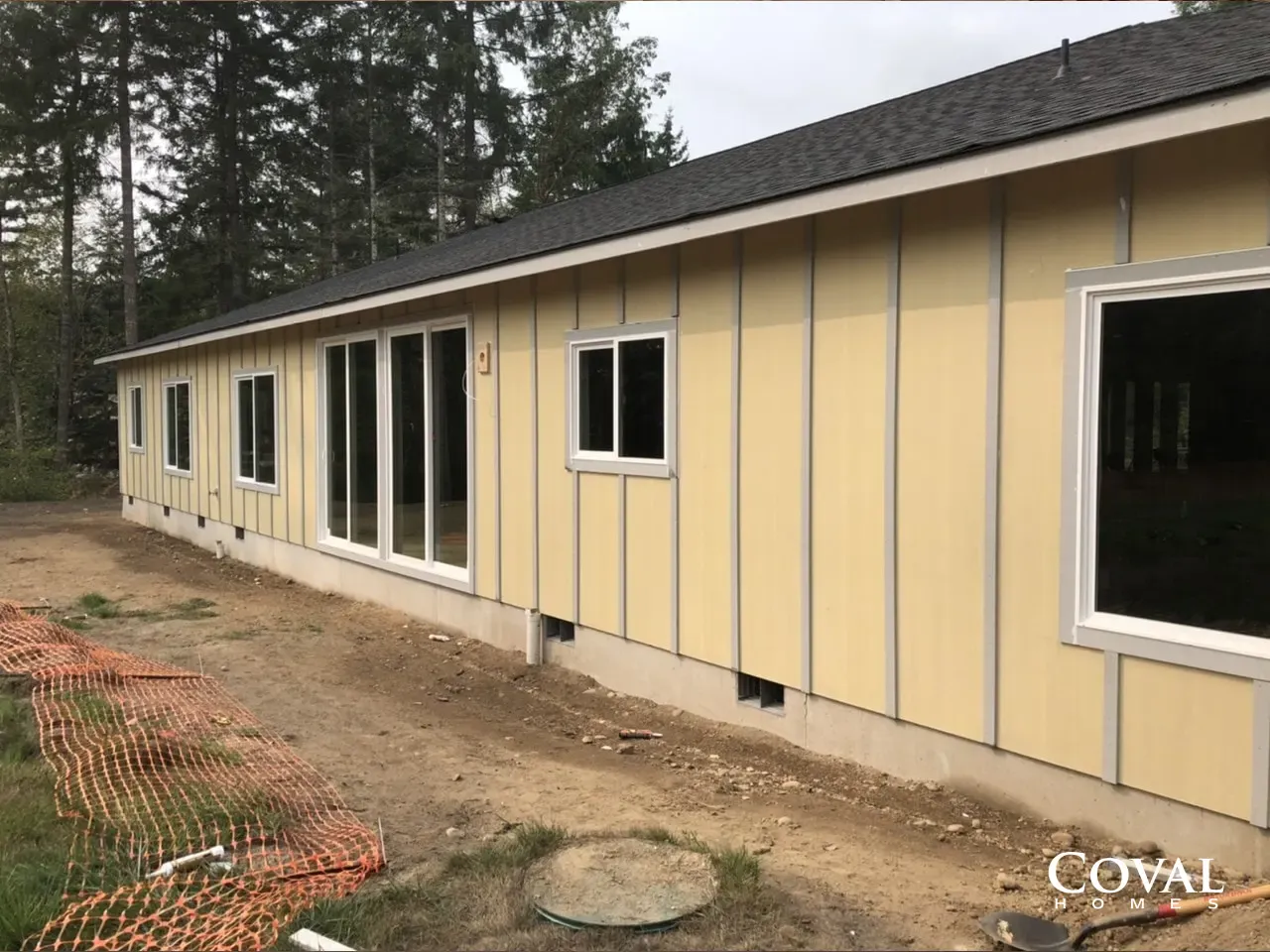 Long yellow modular building with white trim and windows on a dirt lot beside trees