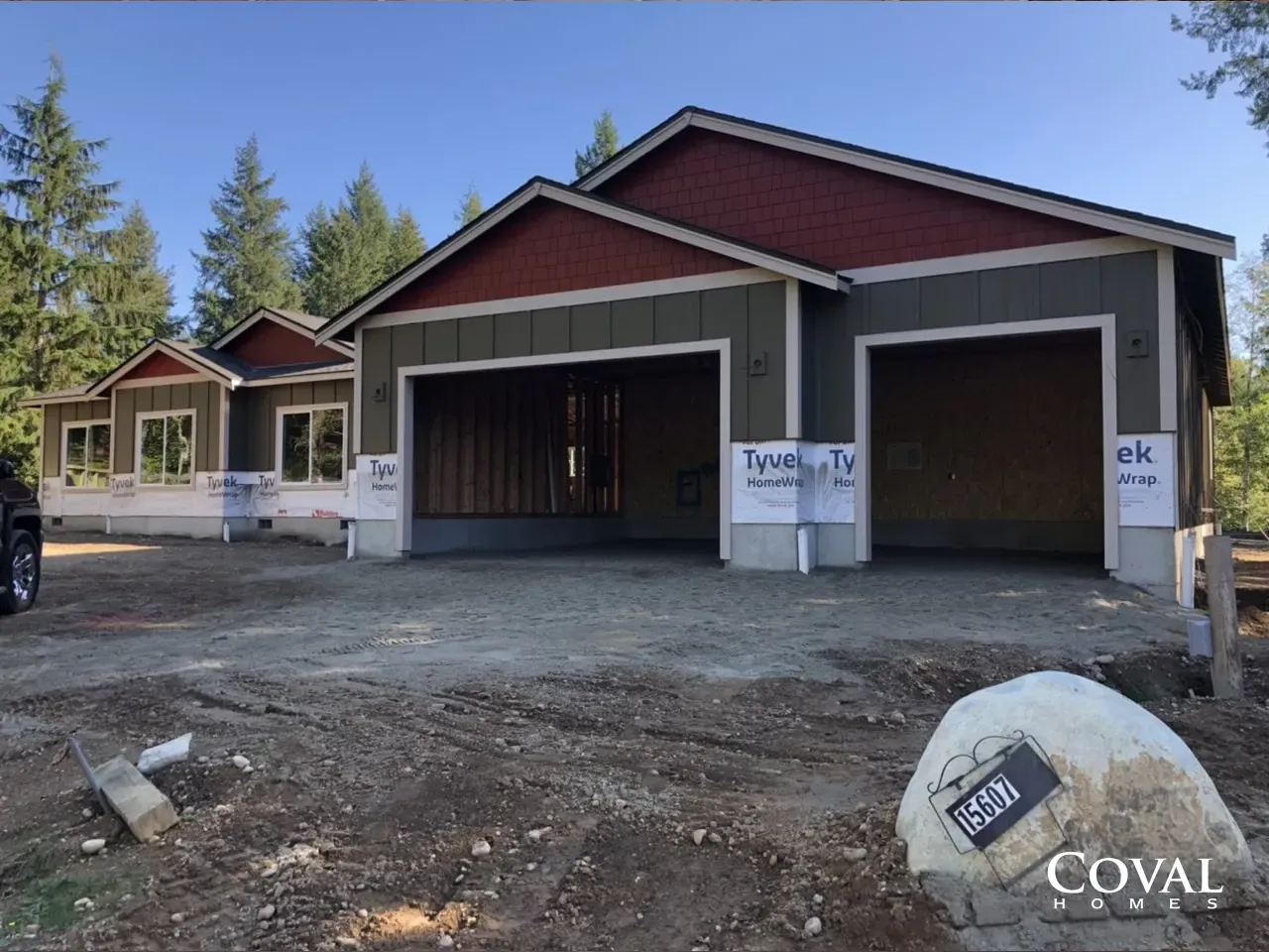 New house under construction with red gables, open garage bays, and dirt foreground