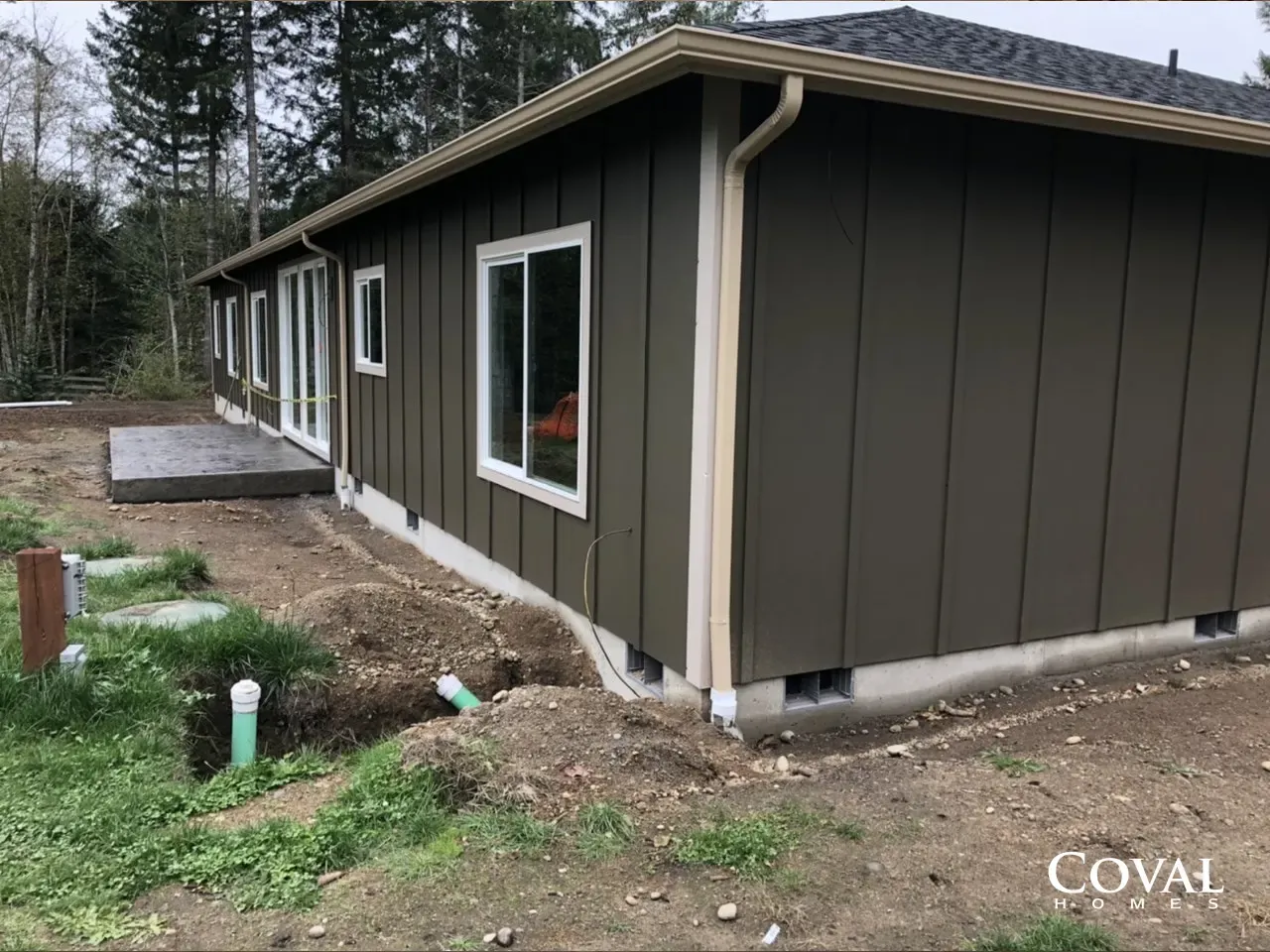 New dark gray house exterior with windows, dirt yard, and white trim under overcast sky