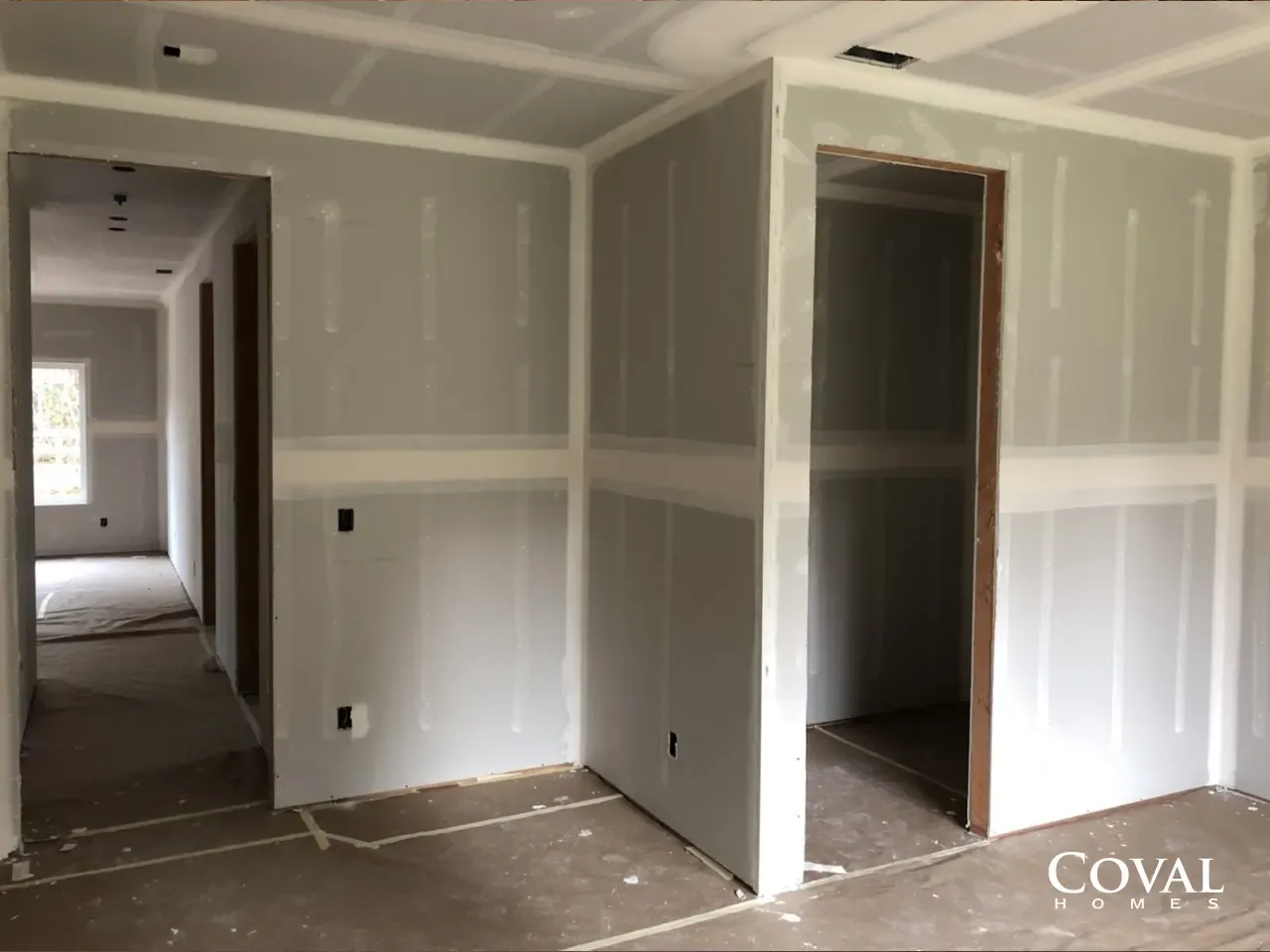 Unfinished drywall interior with open doorways, white walls, and bare concrete floor.