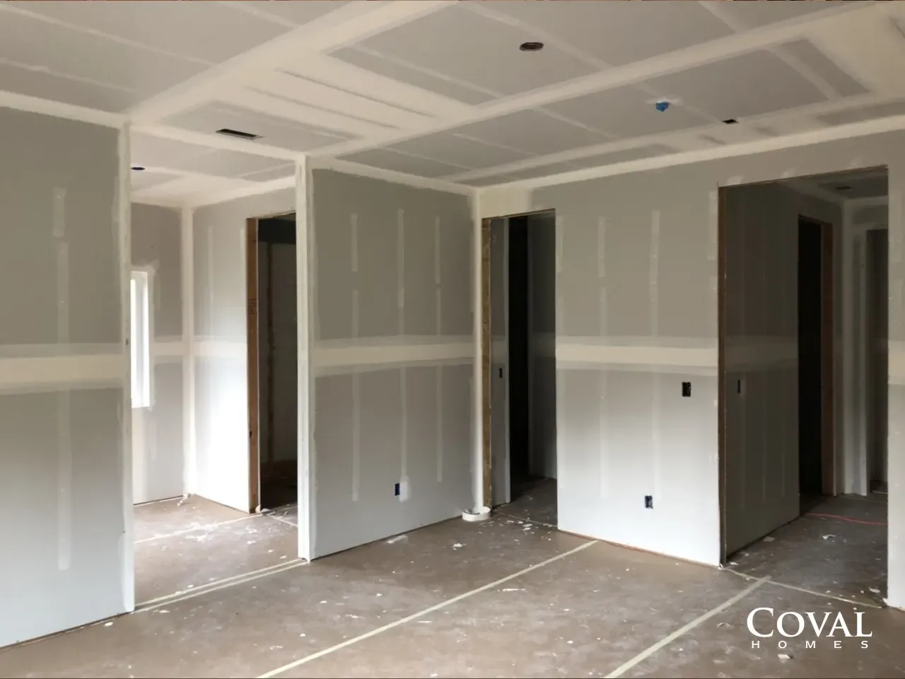 Interior of an unfinished room with drywall, exposed seams, and bare concrete floor under construction