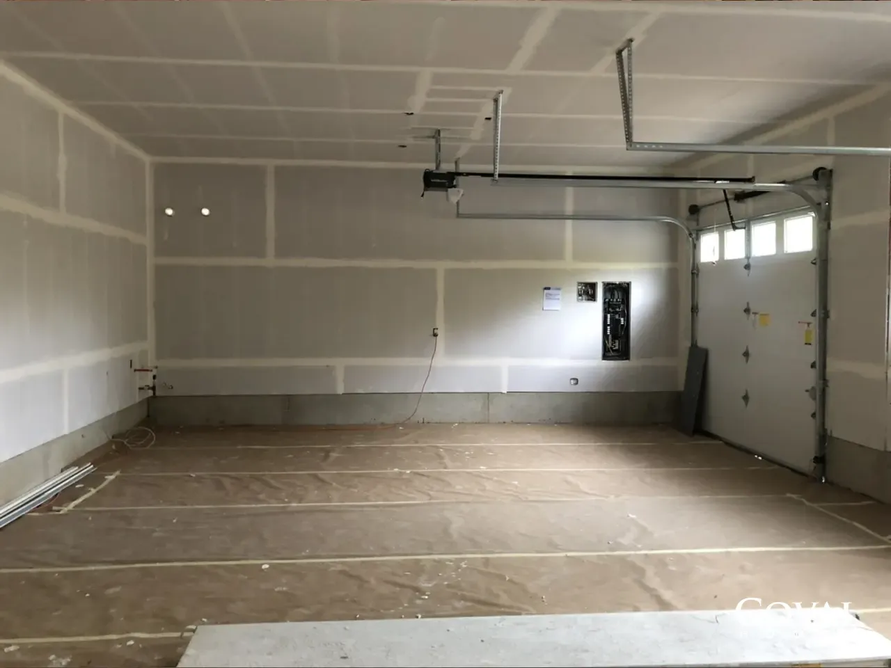 Empty unfinished garage interior with drywall, taped seams, and a closed garage door
