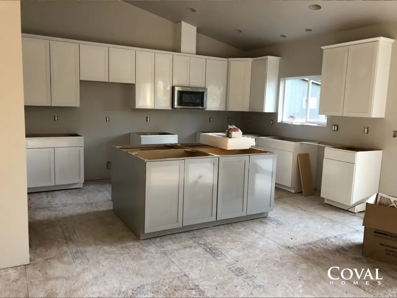 Unfinished kitchen with white cabinets, gray island, and carpeted floor under renovation.
