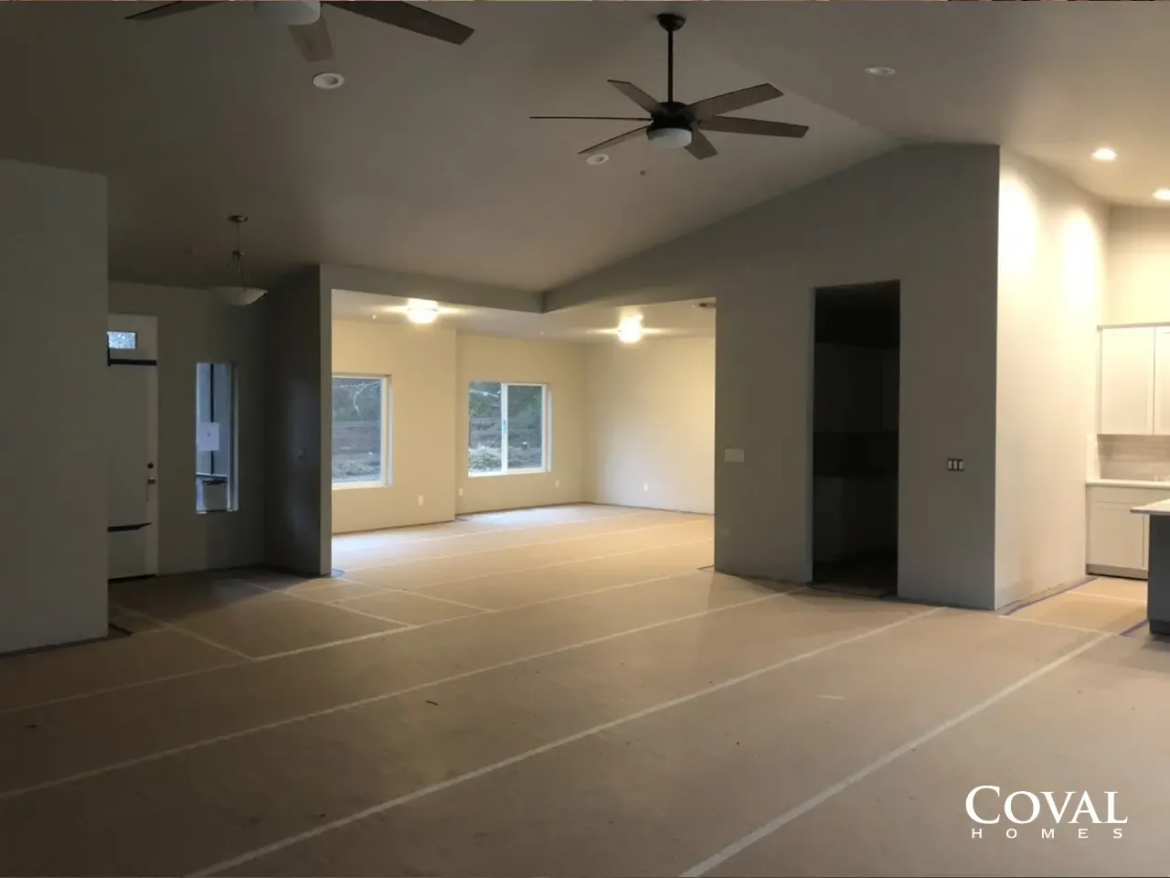 Empty open-plan living room with recessed lights, ceiling fans, and large windows under construction
