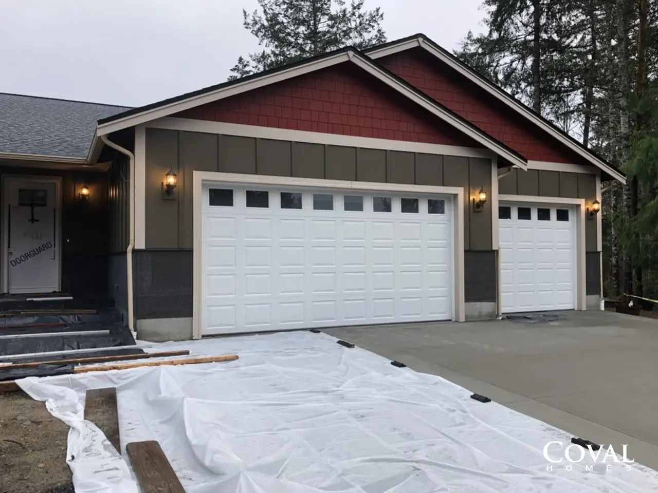 New home with white garage doors and red gable, driveway being covered with white protective tarp