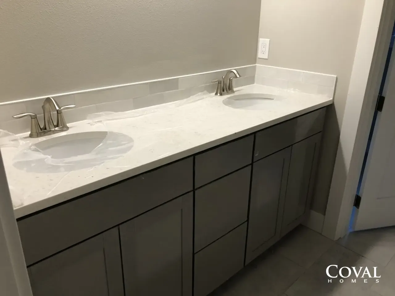 Double vanity bathroom sink with white countertop and dark gray cabinets in a modern restroom
