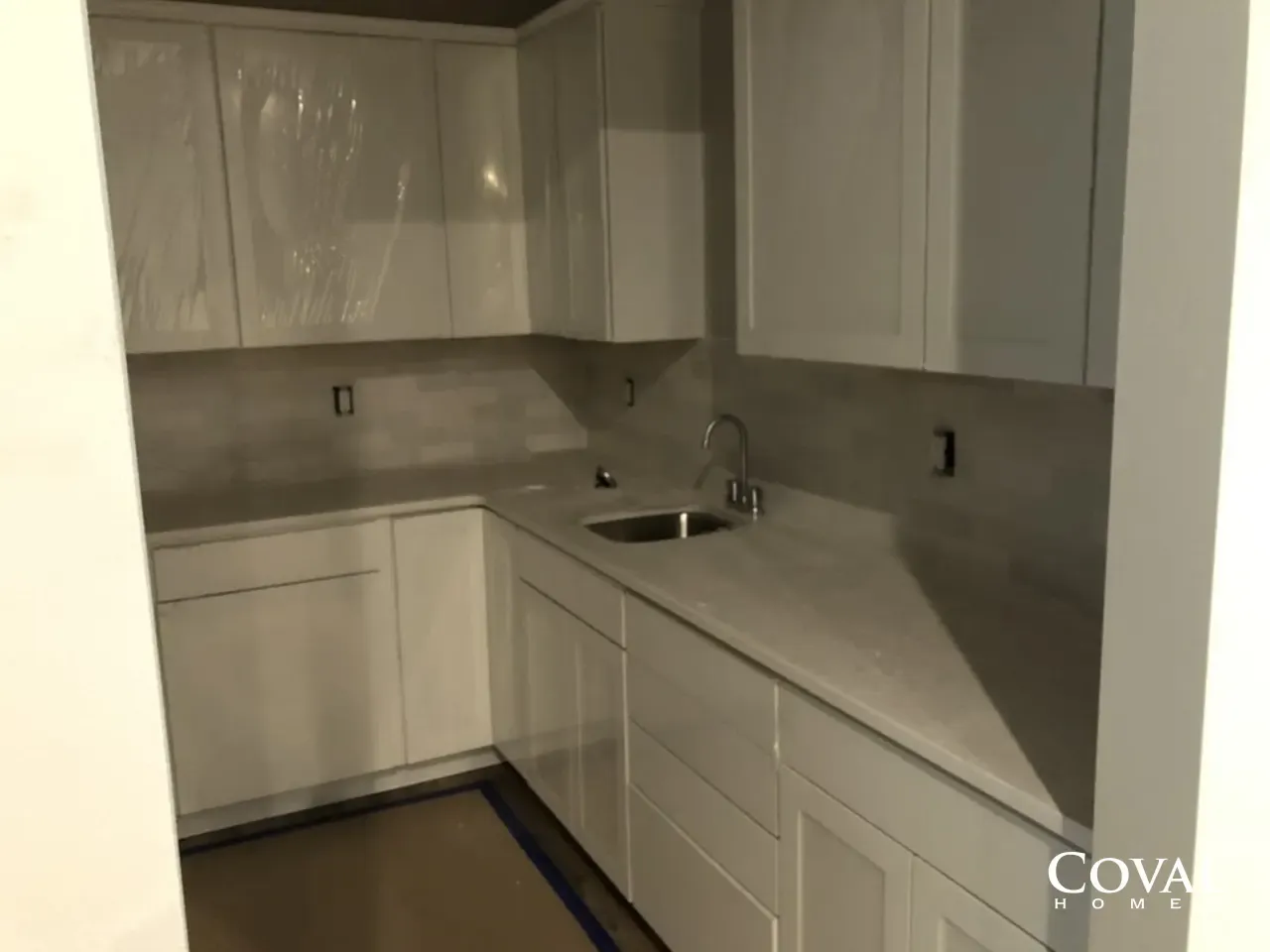 Small modern kitchen with white cabinets, gray countertops, and a stainless sink under dim lighting