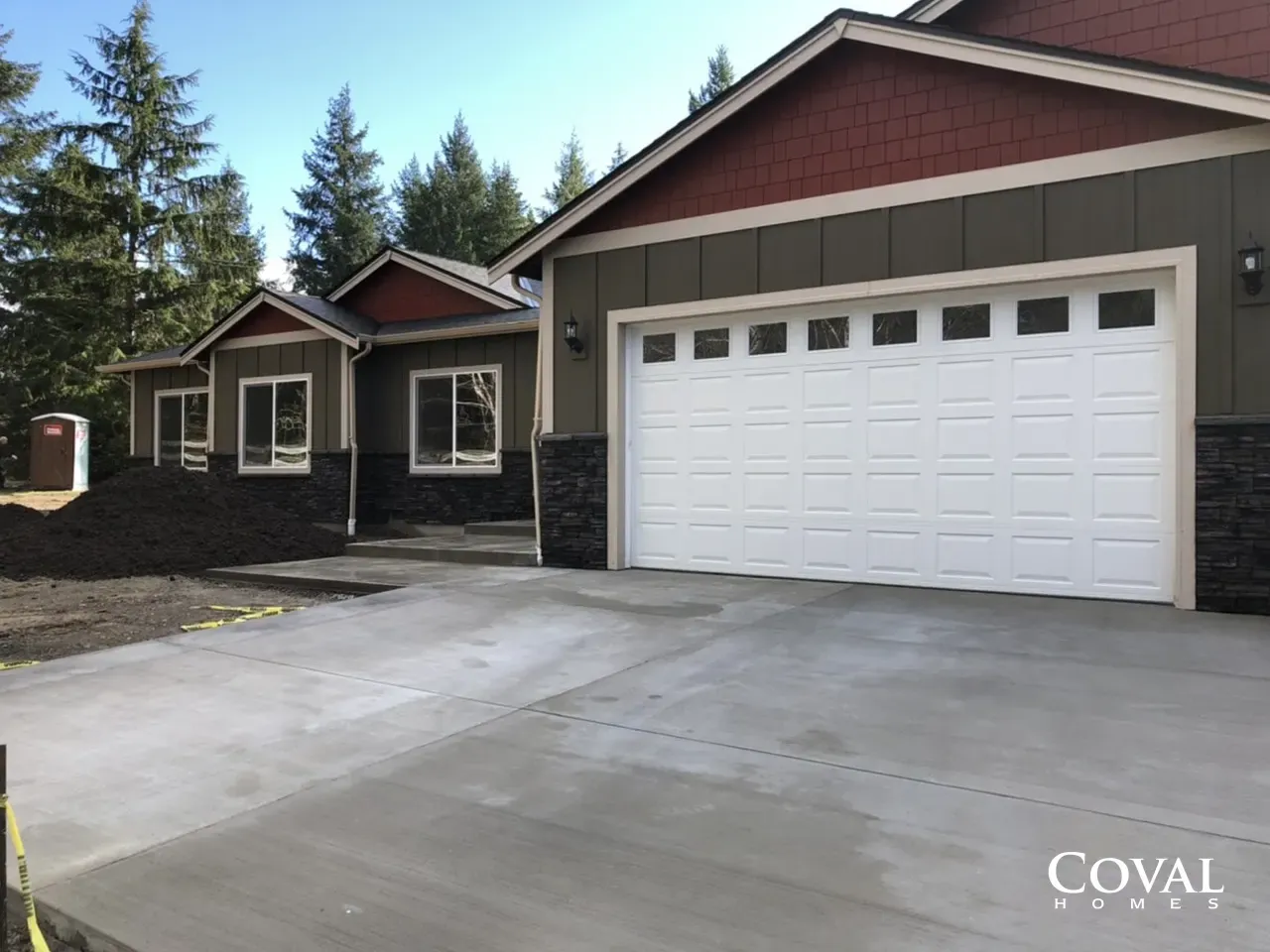 Single-story house with a white garage door and concrete driveway, surrounded by trees.