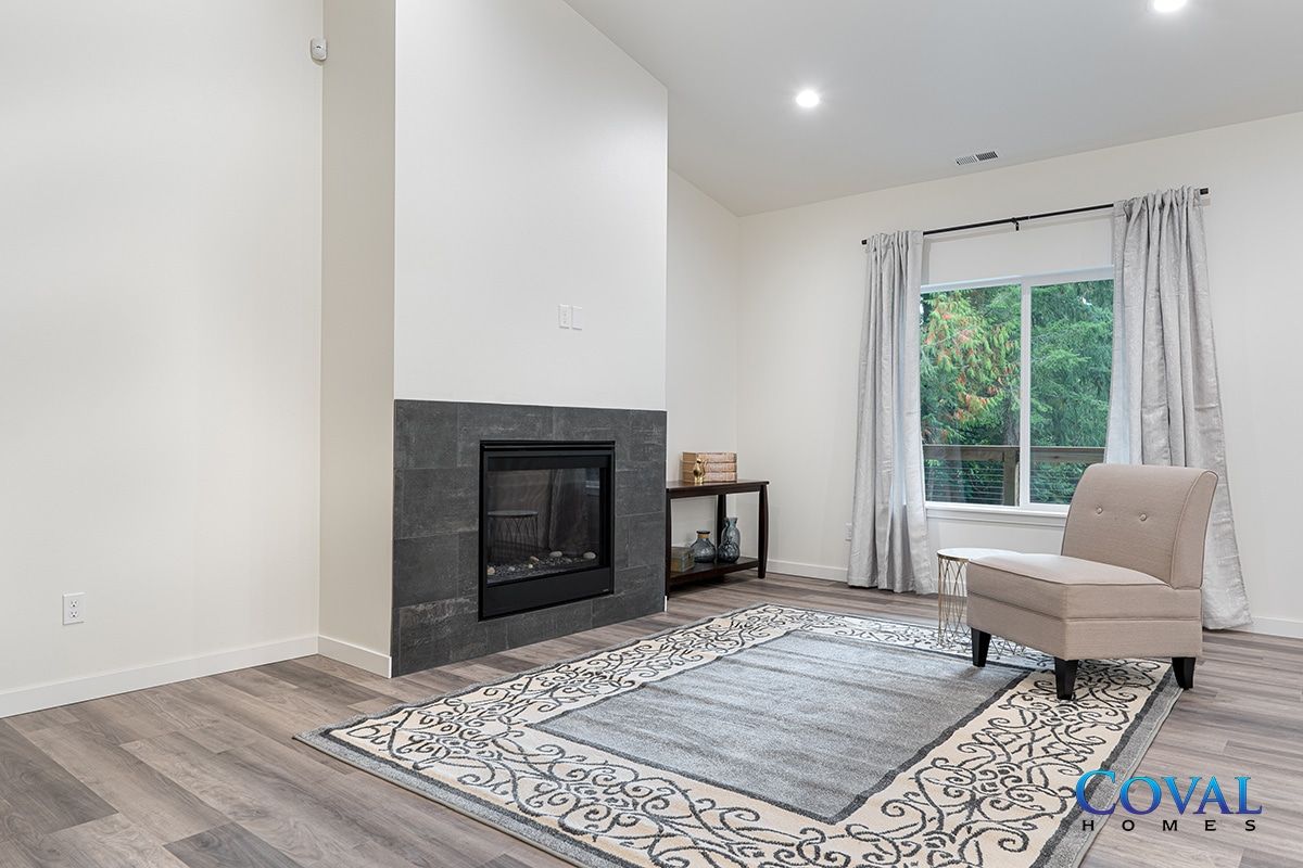 Bright living room with fireplace, patterned rug, chair, and large window with curtains