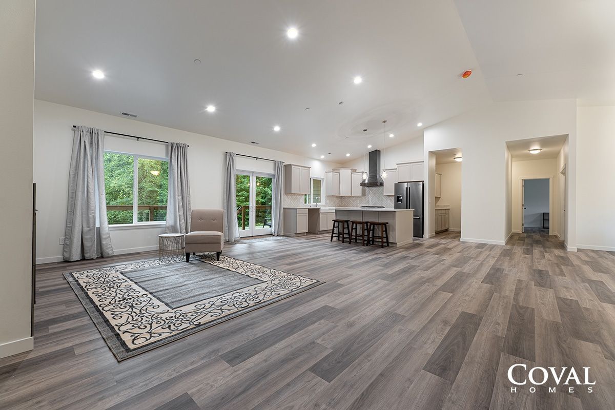 Bright open living room with gray floors, white walls, large windows, rug, and kitchen island.