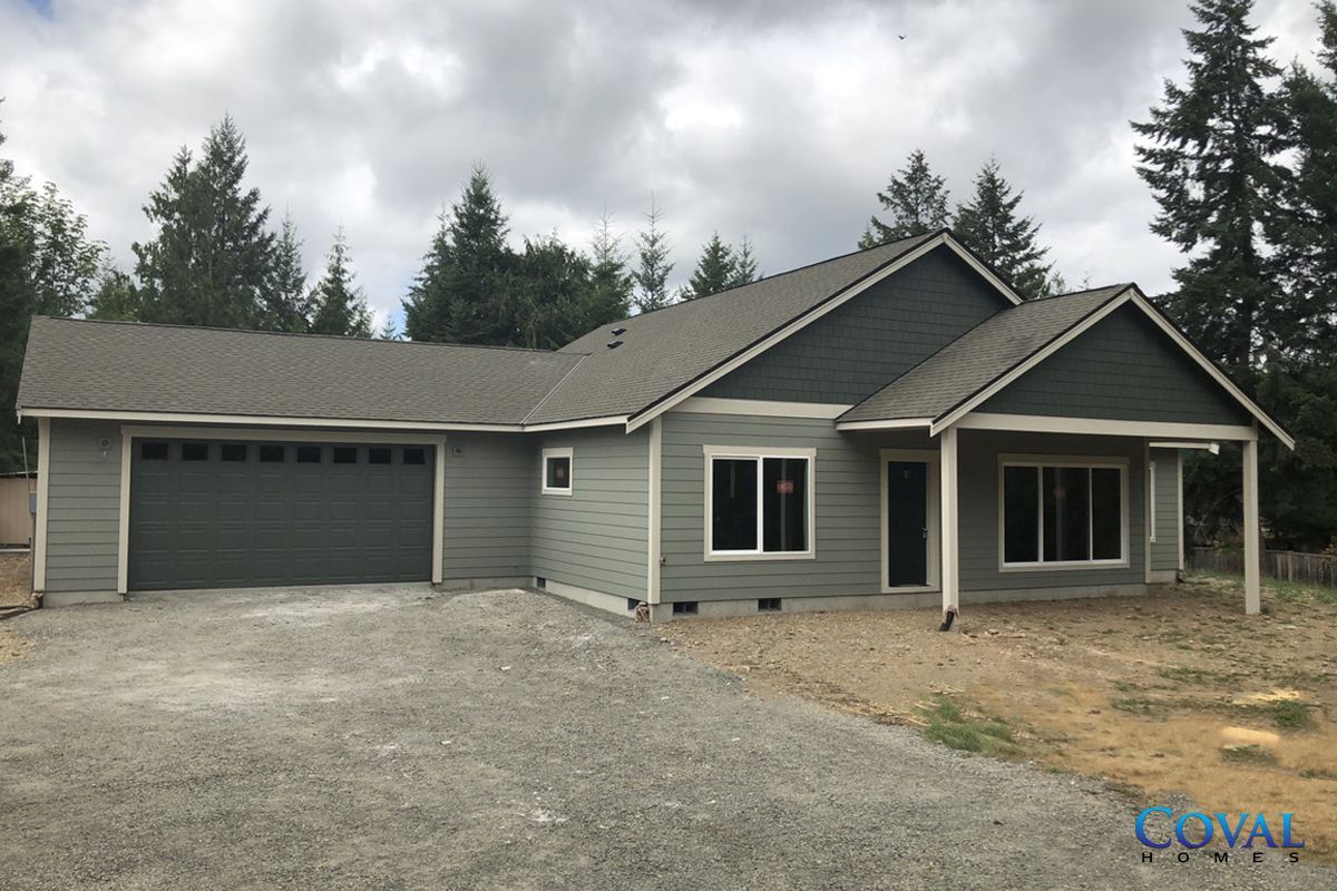 Single-story gray house with attached garage, gravel driveway, and covered front porch under cloudy skies