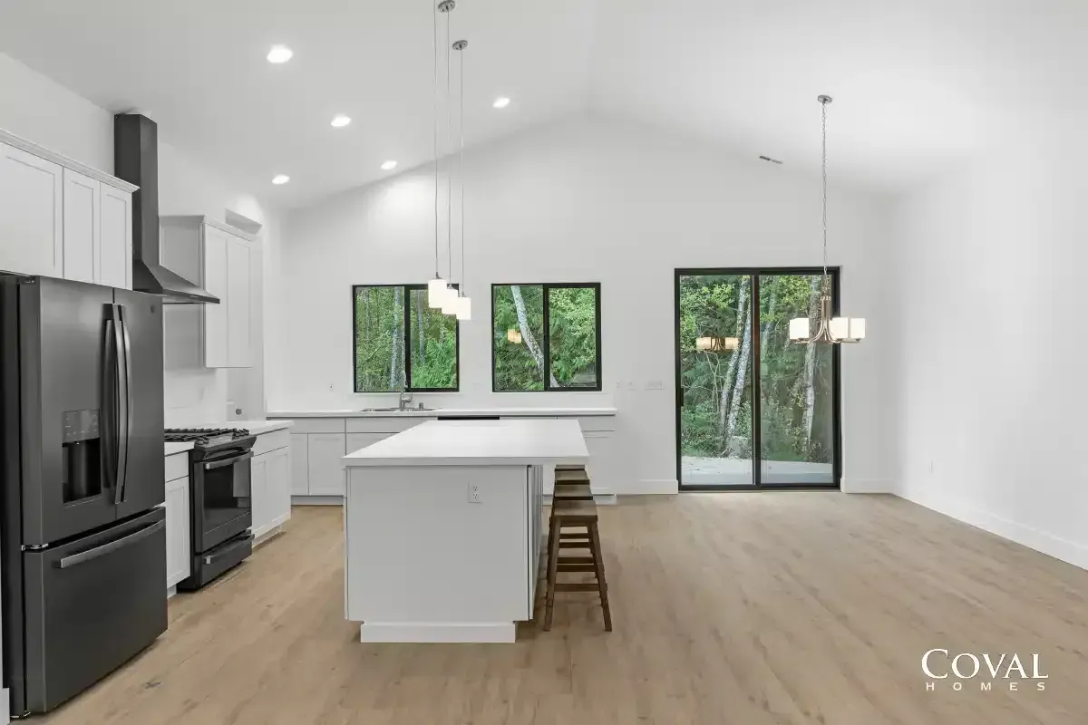 Bright modern kitchen with white cabinets, island, black appliances, and sliding glass doors to greenery