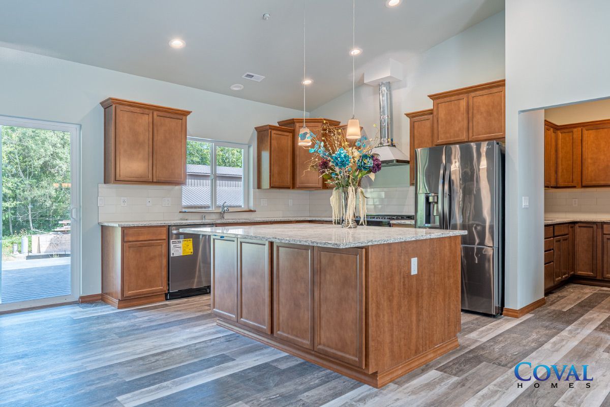 Bright modern kitchen with wood cabinets, granite island, stainless steel fridge, and large windows