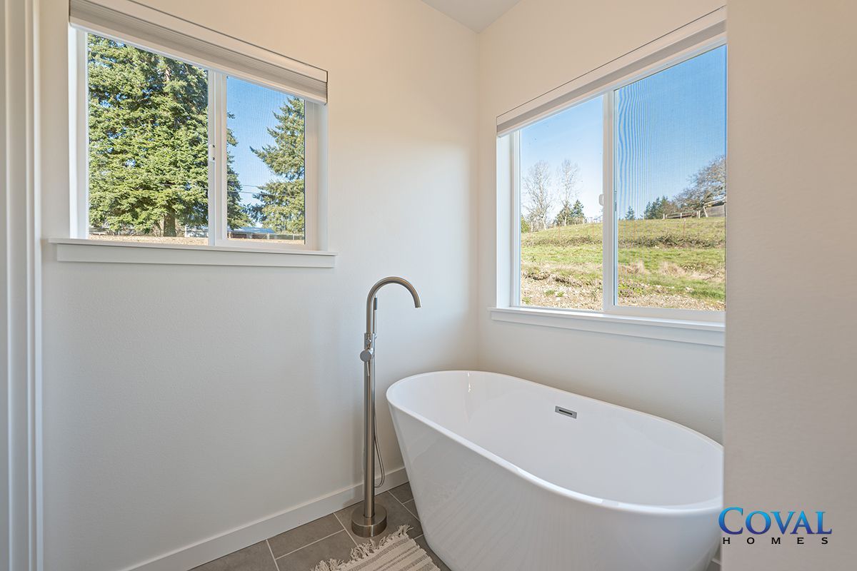 Bright white bathroom with a freestanding tub and two windows overlooking greenery