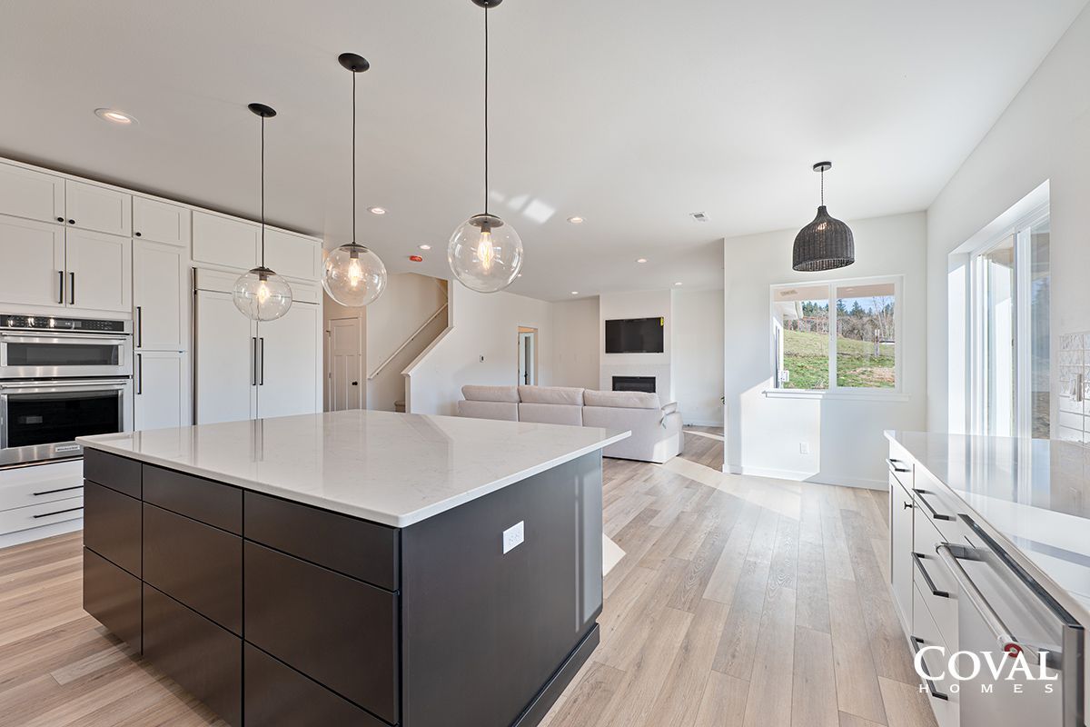 Bright modern kitchen with white cabinets, dark island, pendant lights, and open living area