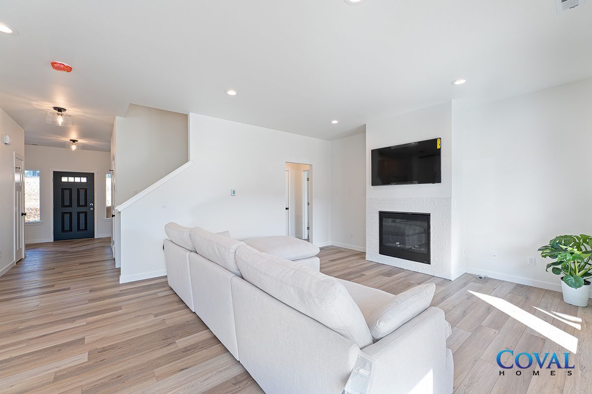 Bright open living room with white sectional, wall-mounted TV, fireplace, and wood floors