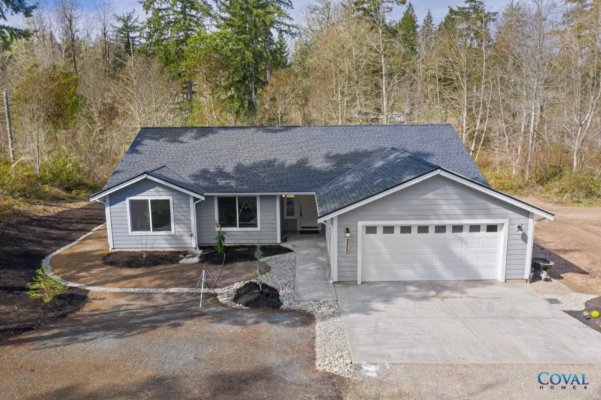 Single-story gray house with attached two-car garage and paved driveway, surrounded by bare trees