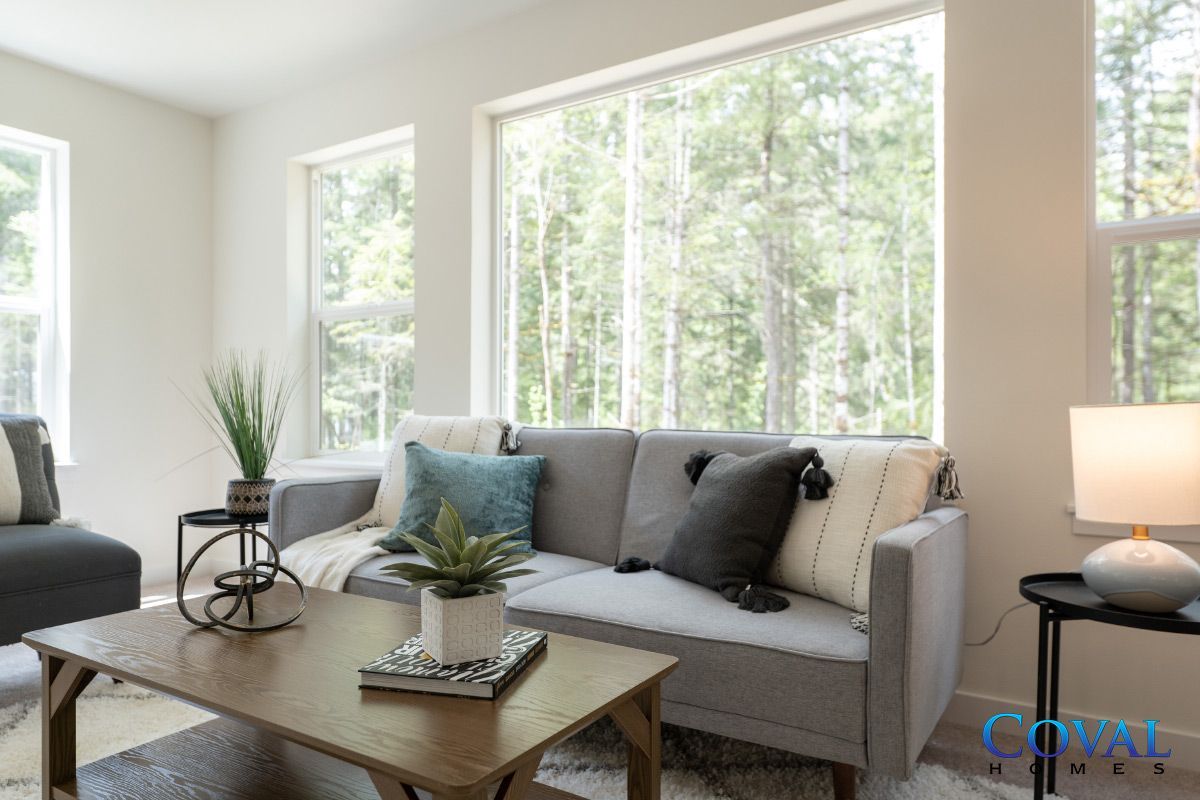 Bright living room with gray sofa, wooden coffee table, and large windows overlooking trees